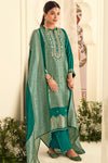 Woman wearing a green embroidered traditional outfit with a dupatta in an elegant setting.