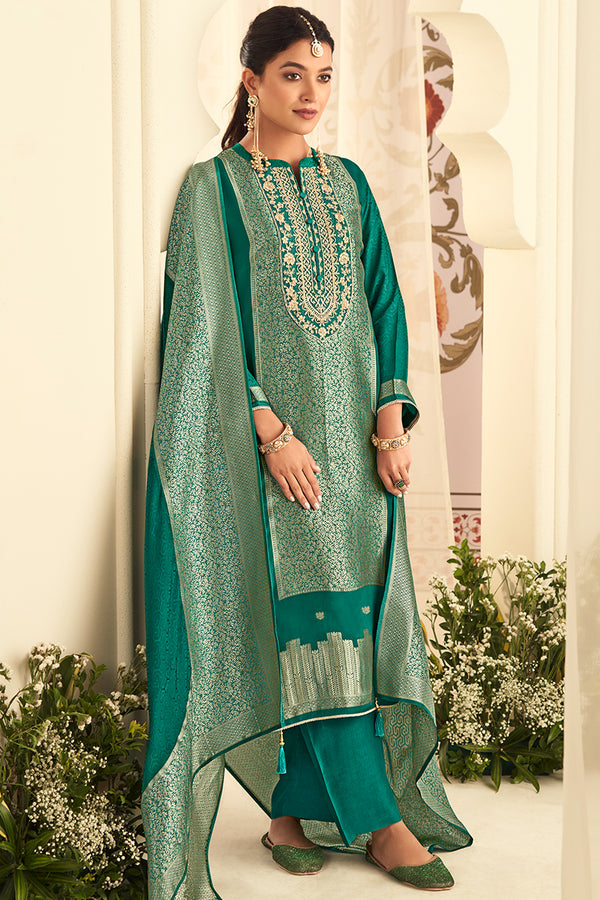 Woman wearing a green embroidered traditional outfit with a dupatta in an elegant setting.